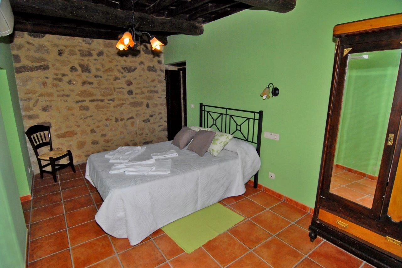 Dormitorio con pared de piedra, vigas de madera y cama doble · Casa Rural Sietevillas