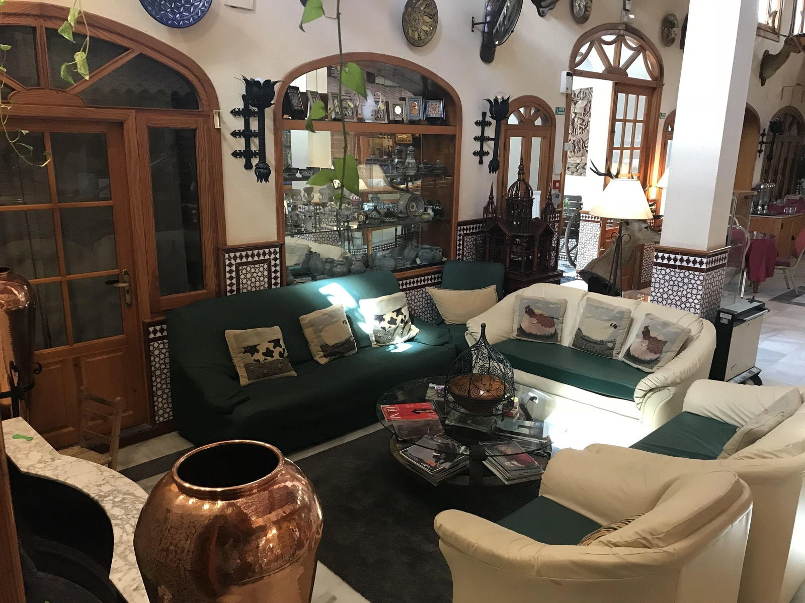 Salón del Hotel El Paso con sofás, arcos y objetos de cobre · Hotel El Paso