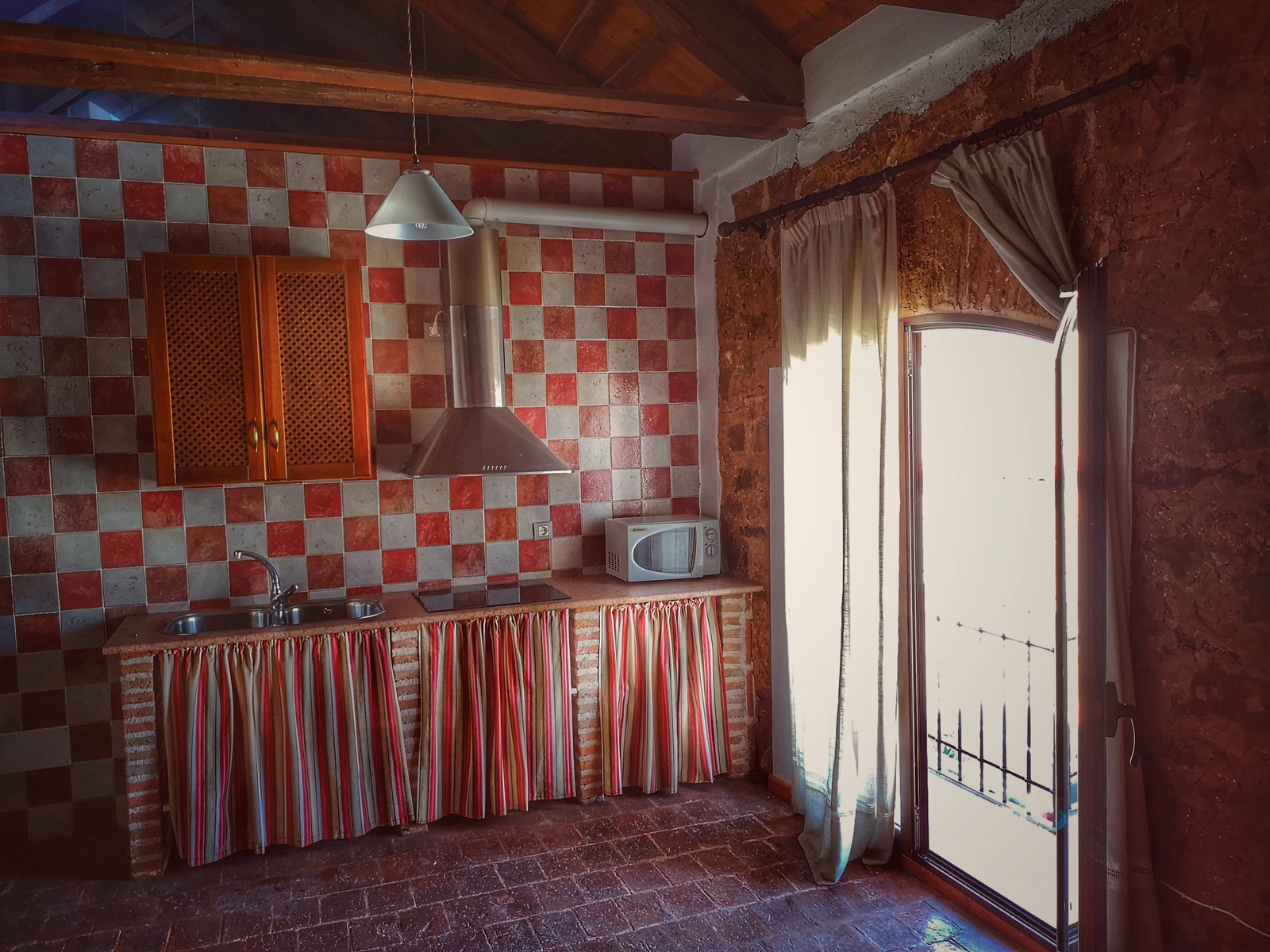 Cocina con alicatado rojo y blanco, muebles de madera y ventana al exterior. · Casa Rural Hidalgo