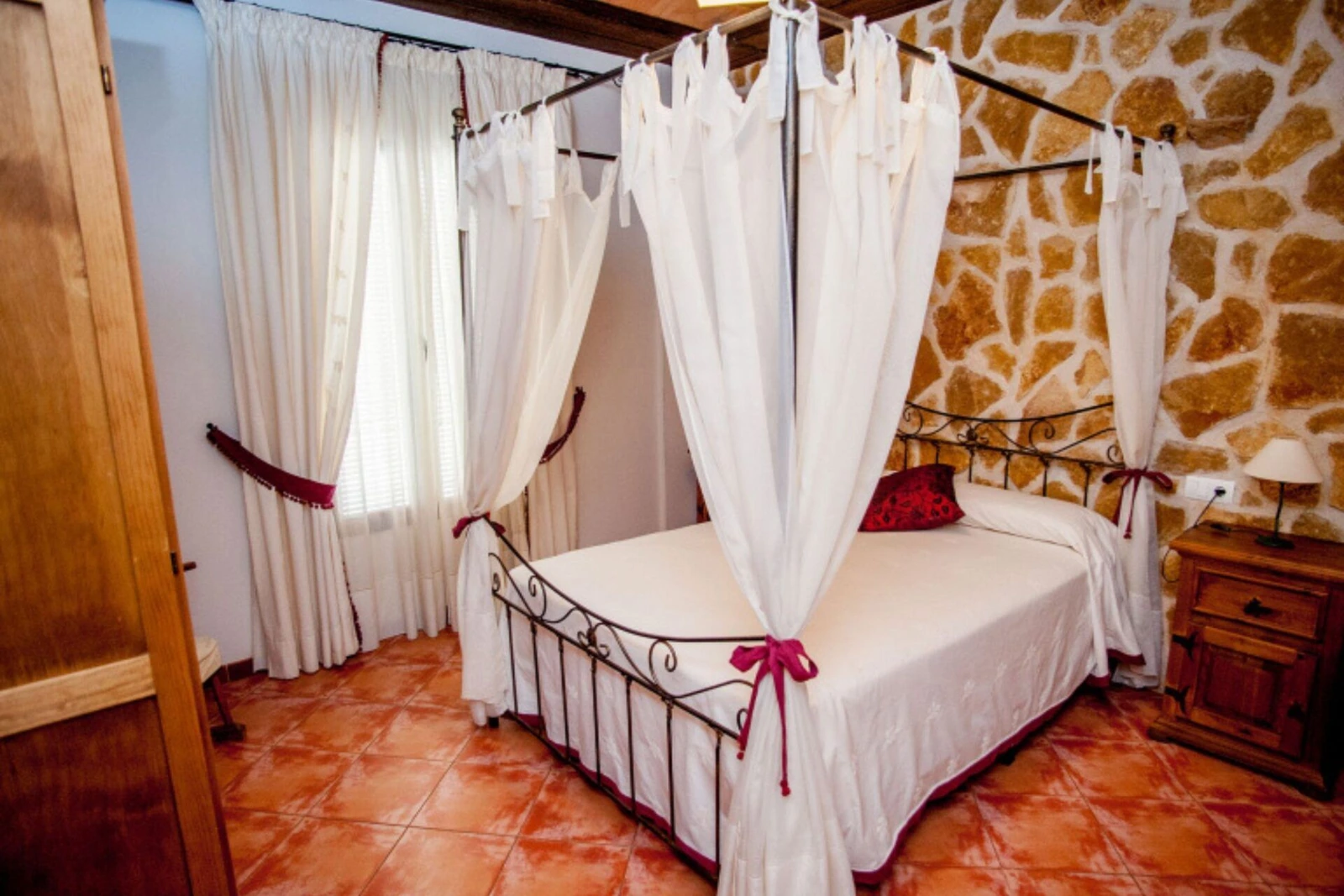 Dormitorio de matrimonio con dosel blanco y pared de piedra. · Casa Rural La Plaza