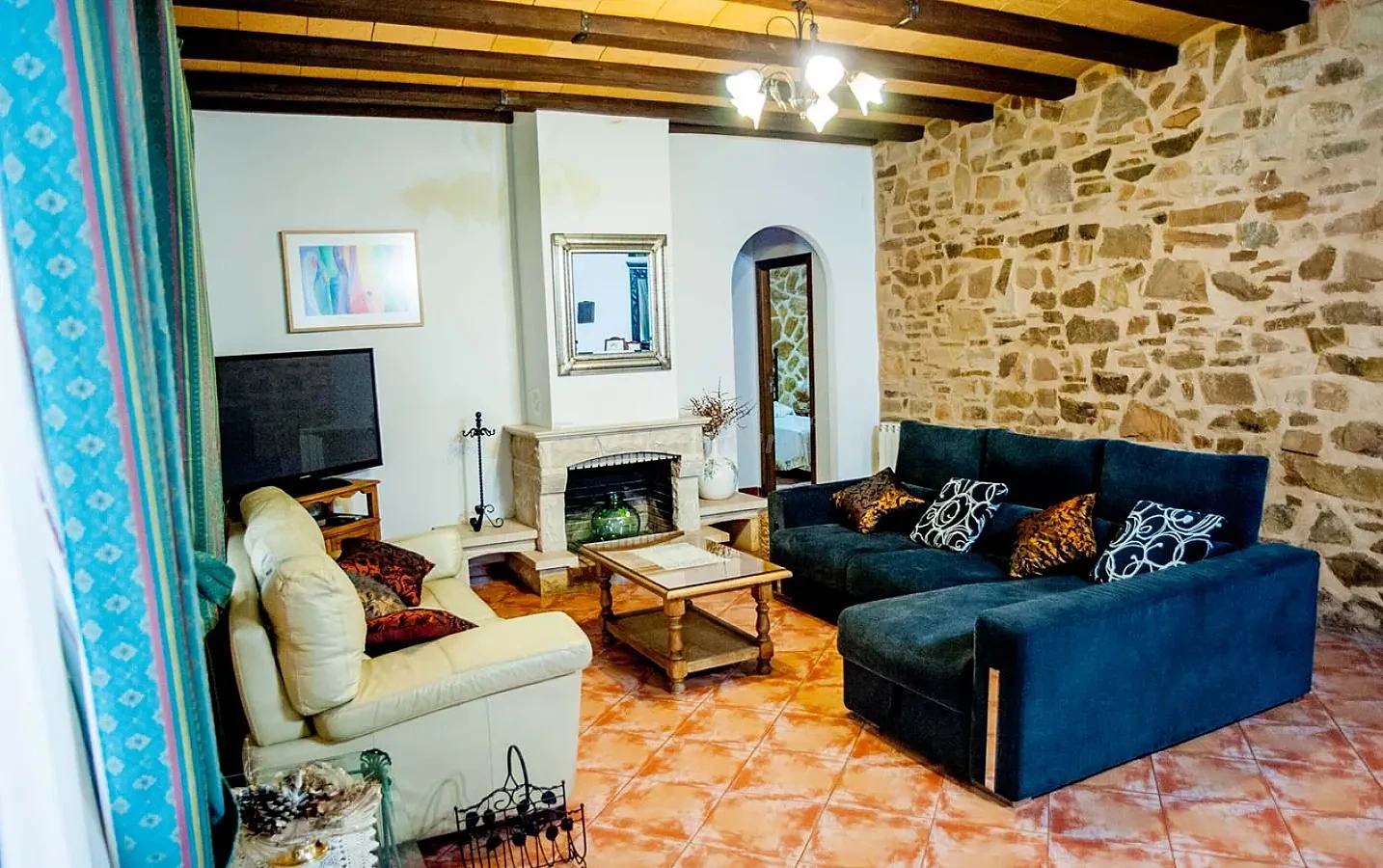Salón con chimenea, sofás azules y blancos y paredes de piedra. · Casa Rural La Plaza