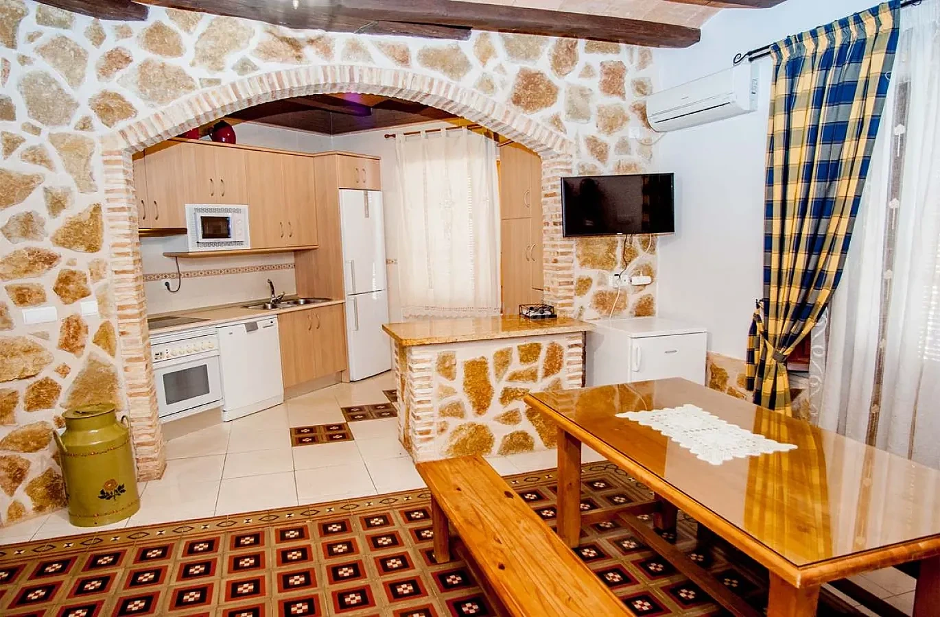 Cocina y comedor con arco de piedra y electrodomésticos blancos. · Casa Rural La Plaza
