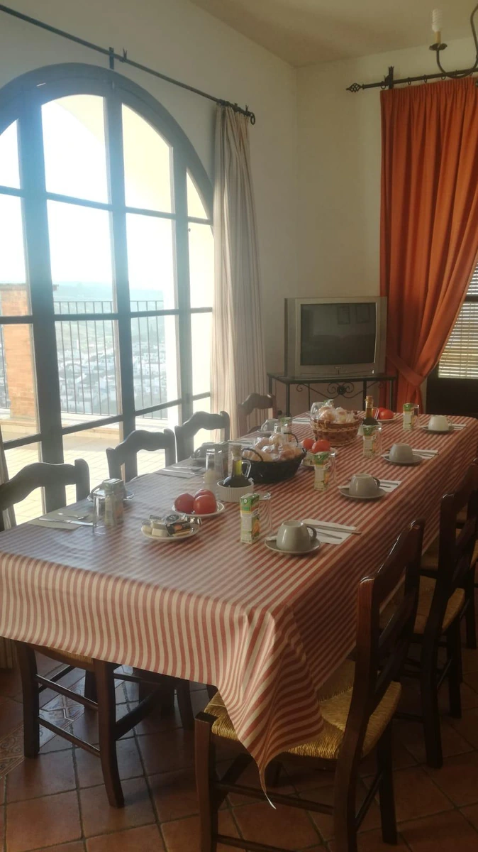 Comedor común con mesa larga junto a ventanales y cortinas rojas. · Casa Maika