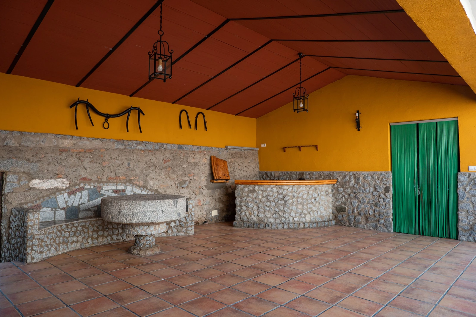 Terraza cubierta con barra de piedra y pared amarilla. · Cortijo Charcollana