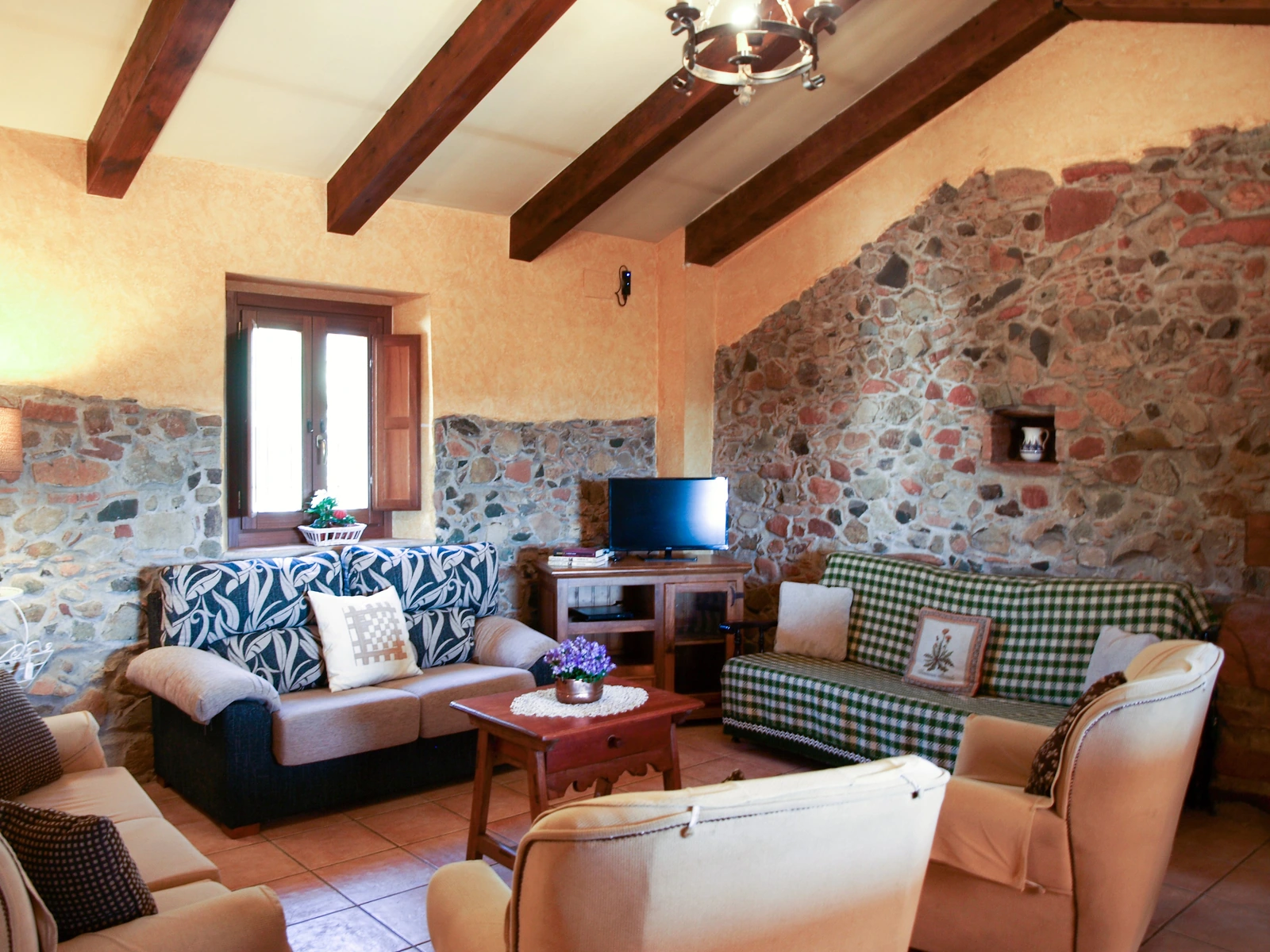Salón con sofá, sillones y paredes de piedra bajo vigas de madera. · Cortijo de Camama