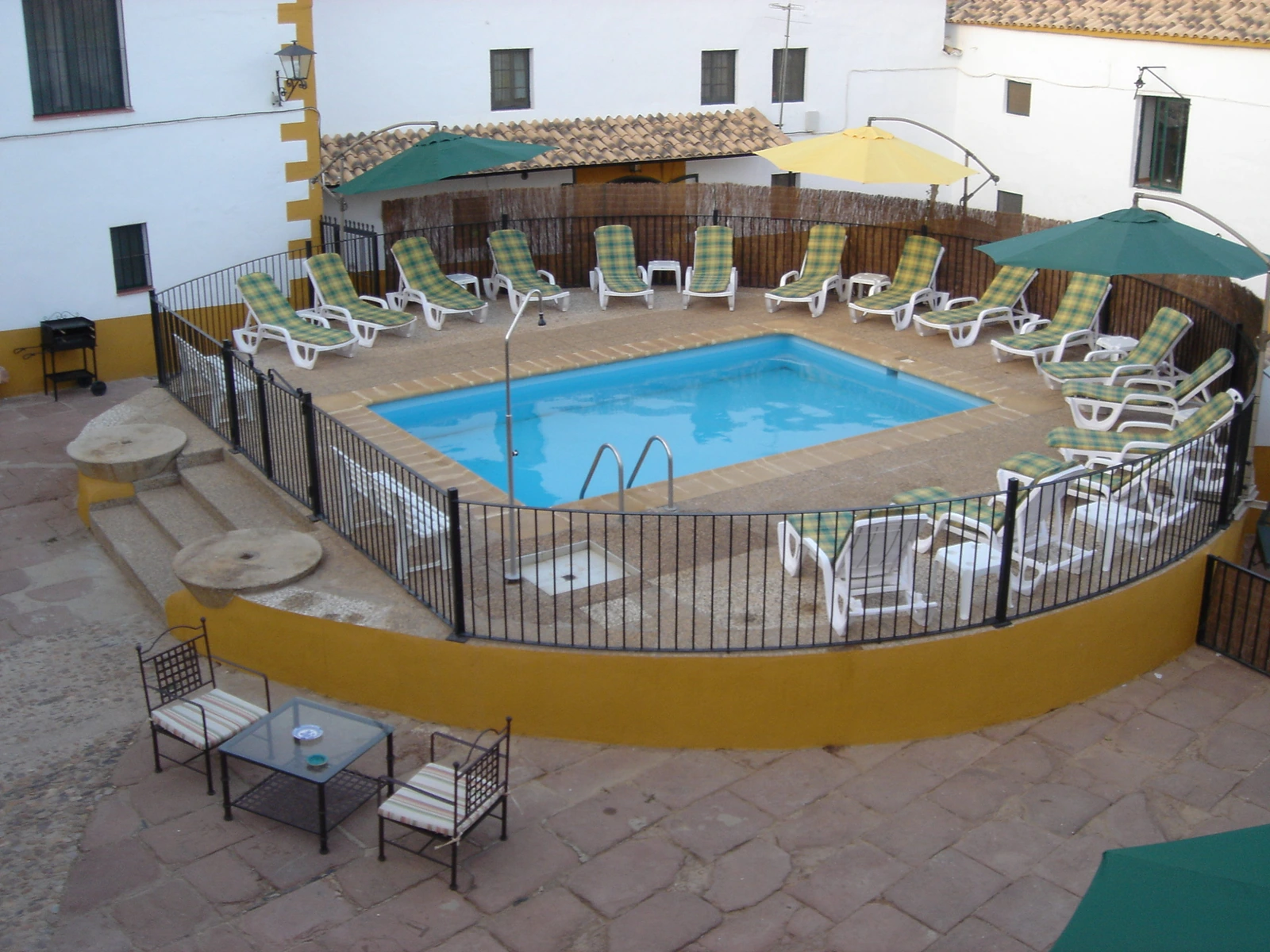 Piscina vallada en el patio central, con tumbonas y sombrillas. · Cortijo Molino San Juan
