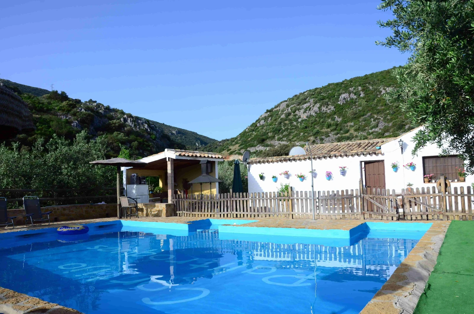 Piscina vallada del cortijo con la casa y el patio al fondo. · Cortijo Palitroques