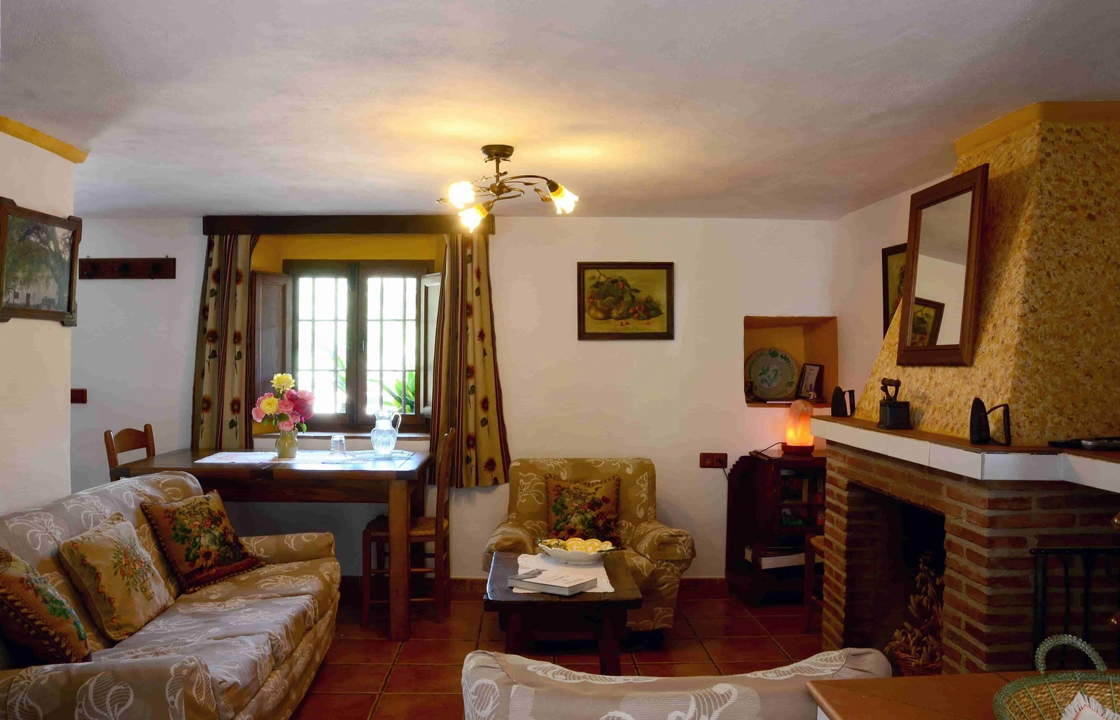 Salón comedor con sofás, chimenea y mesa bajo vigas de madera. · Cortijo Palitroques
