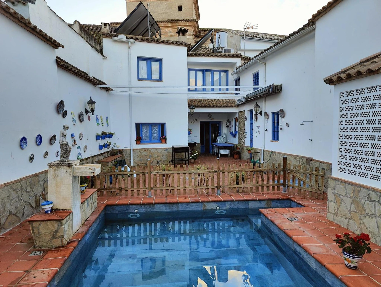 Piscina del patio interior con la fachada blanca y ventanas azules. · La Casa de Maita