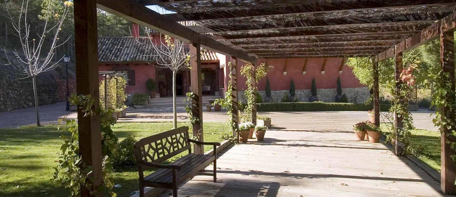 Pérgola y sendero del jardín del hotel con su fachada roja al fondo. · La Casita de Cabrejas