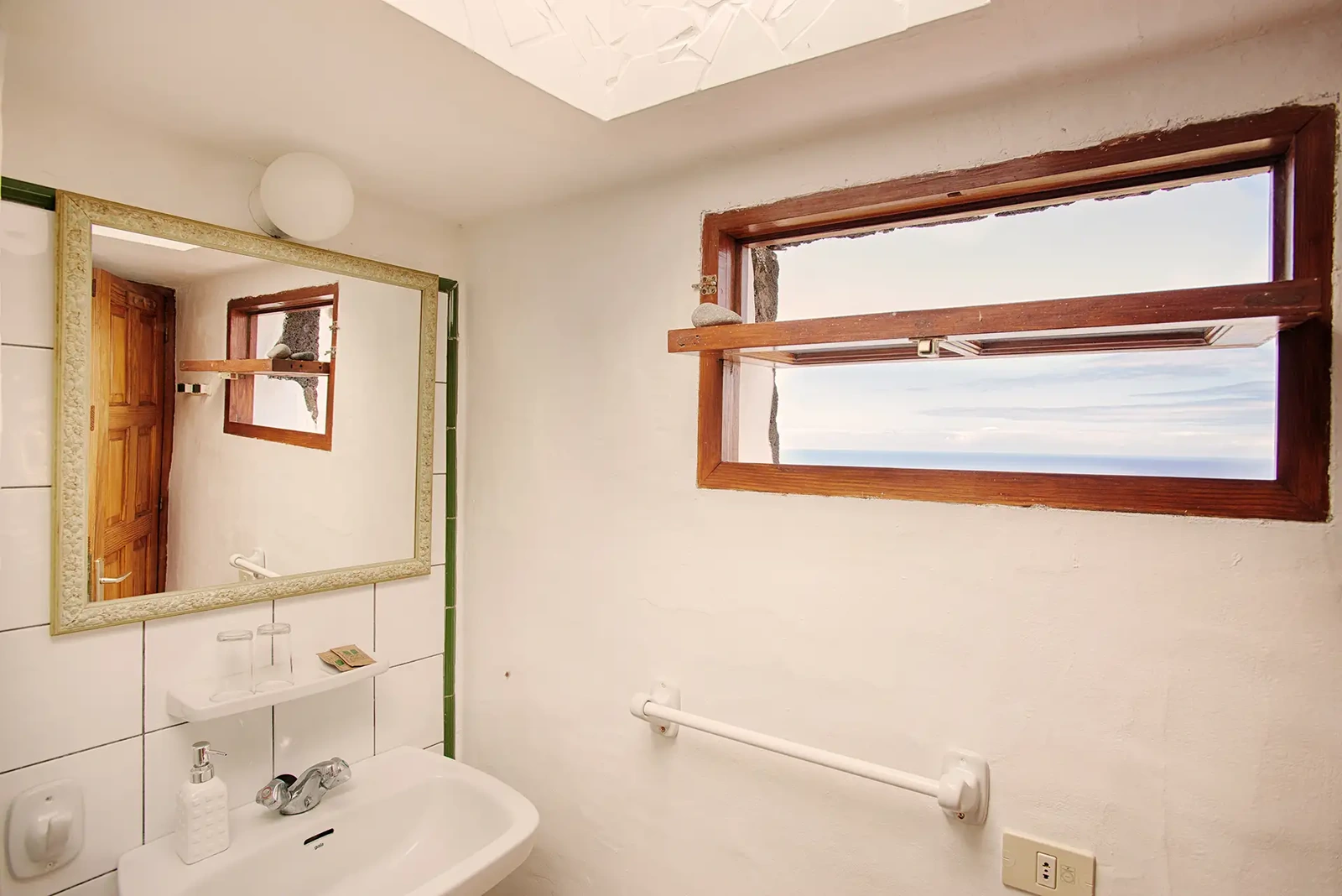 Baño de Sabinosa, con lavabo, espejo y ventana horizontal. · El Sitio