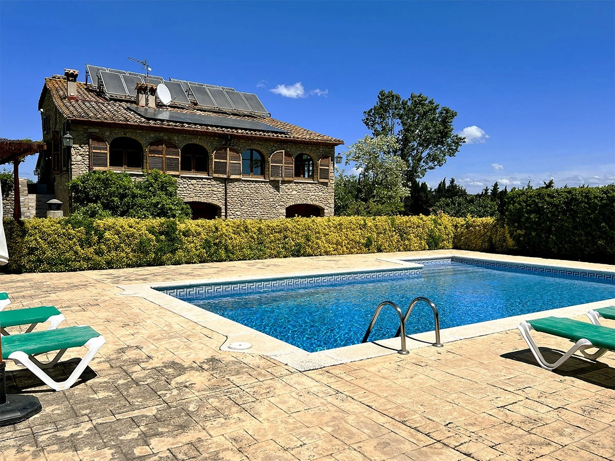 Piscina exterior con tumbonas y la casa al fondo. · Can Masó