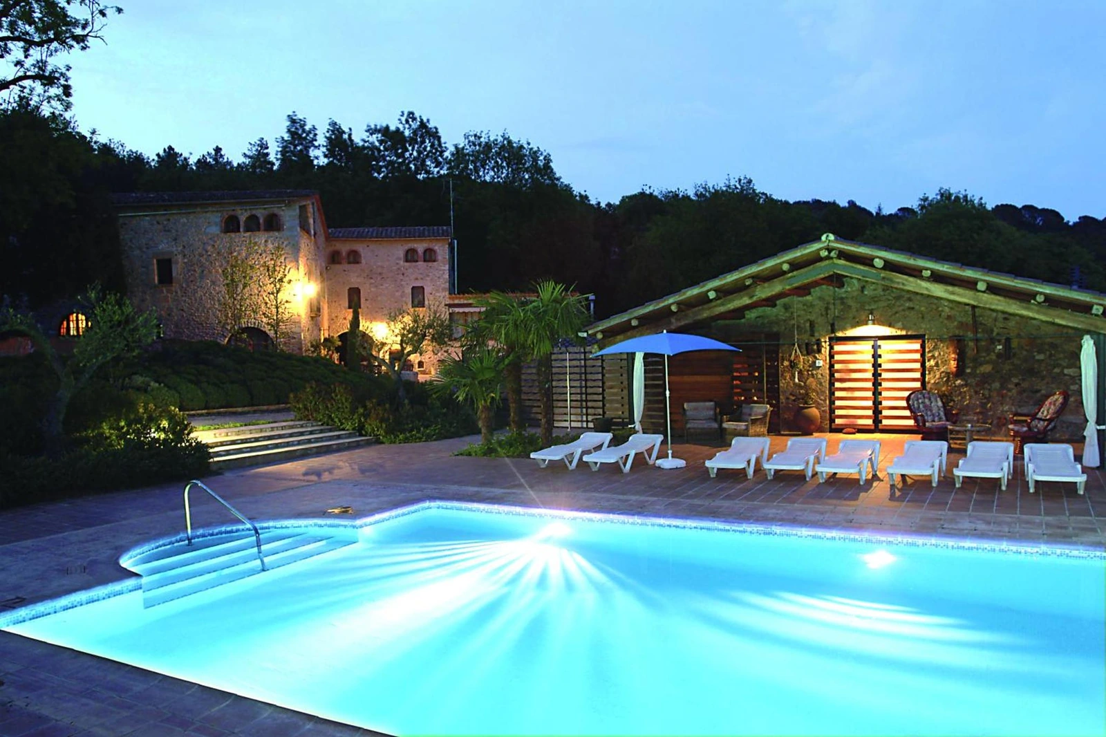 Piscina común y casa iluminadas al atardecer. · Can Vila