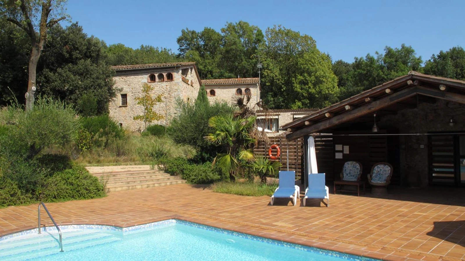 Terraza junto a la piscina común, con dos sillas azules. · Can Vila
