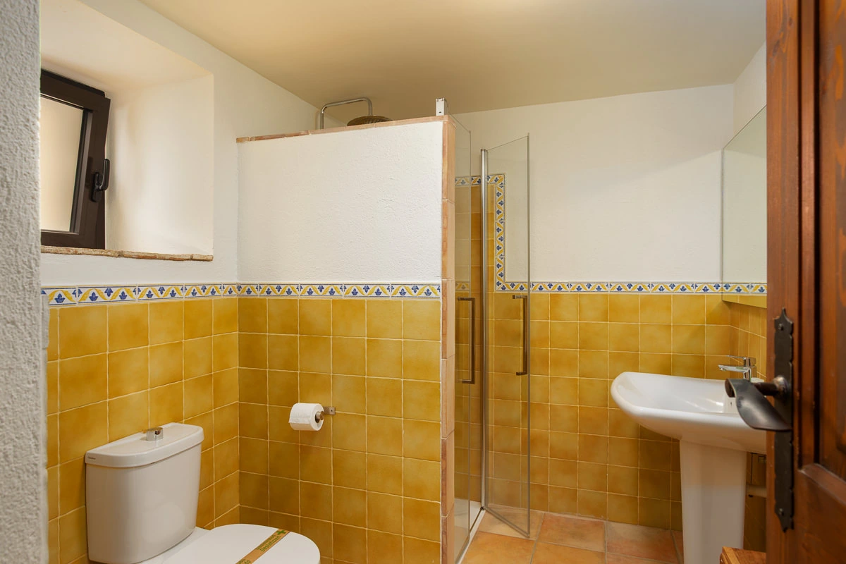 Baño de El Celler, con ducha, lavabo y azulejos amarillos. · El Nus de Pedra