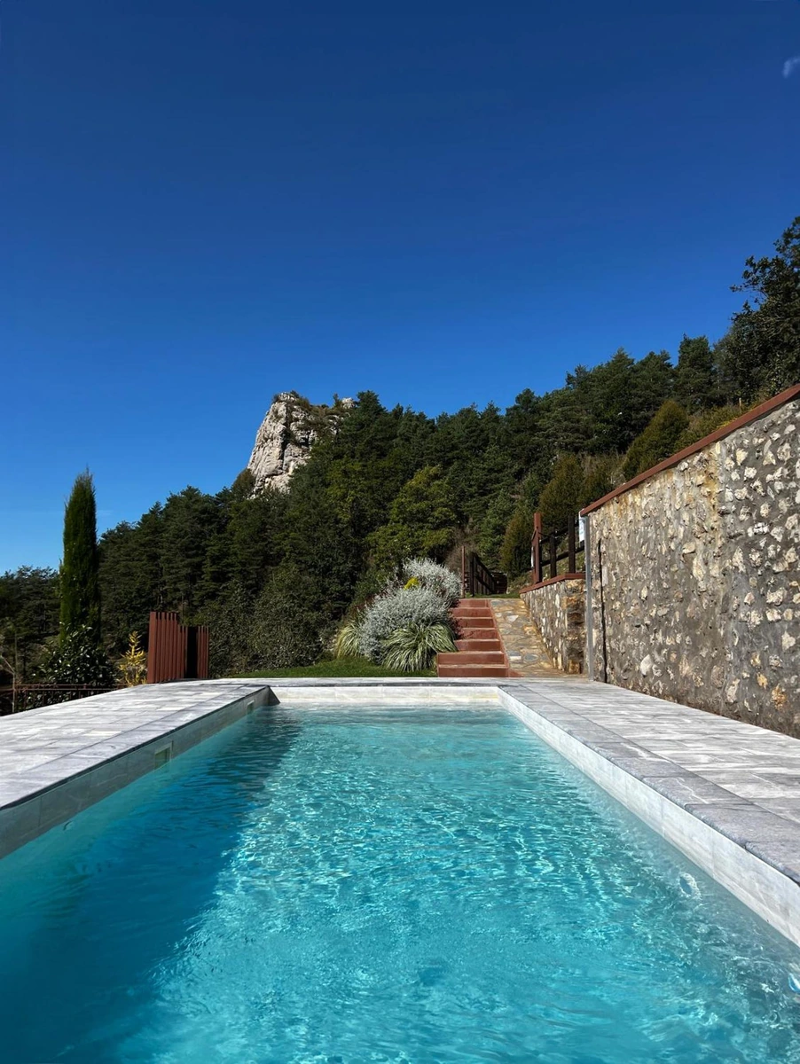 Piscina de Mas Merolla junto al muro de piedra, con vistas a las montañas. · Mas Merolla