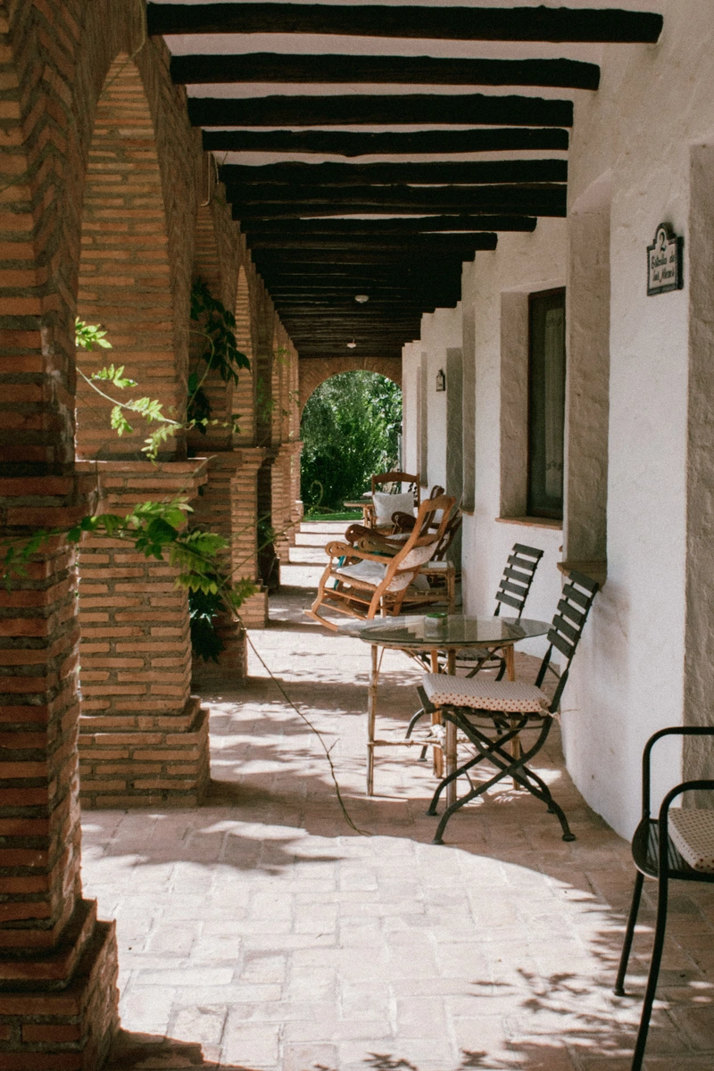 Galería exterior de acceso a las habitaciones, con mesas y sillas. · Alquería de Los Lentos