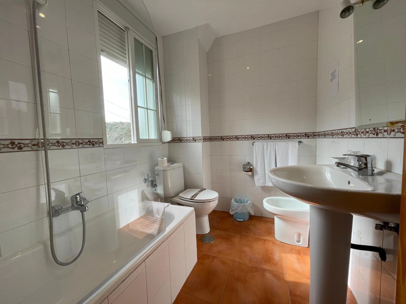 Baño del hotel con bañera, mampara, lavabo y ventana. · Quéntar Hotel Rural