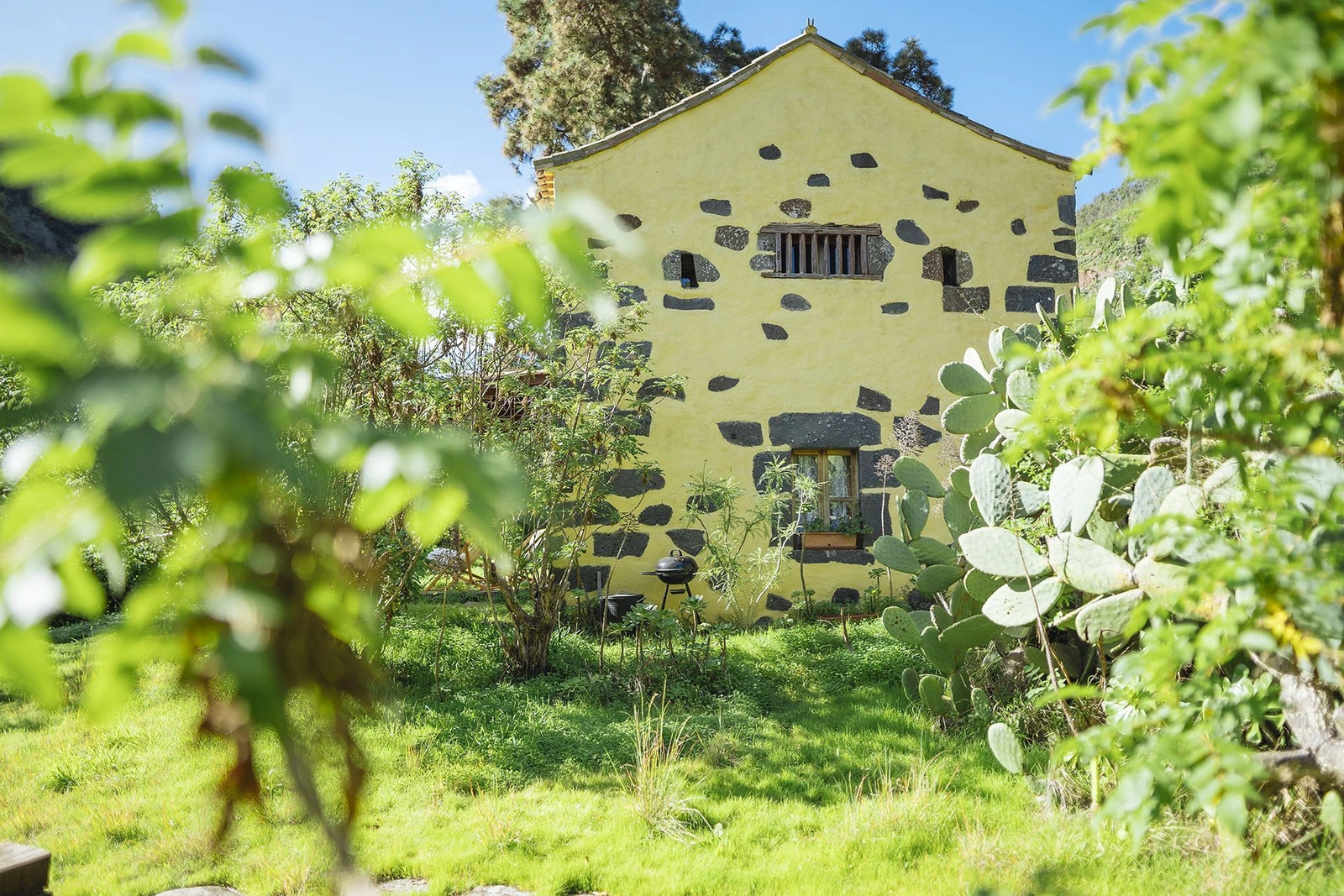 El Pajar: fachada de piedra y revoco entre plantas del jardín. · Finca Casa de La Virgen
