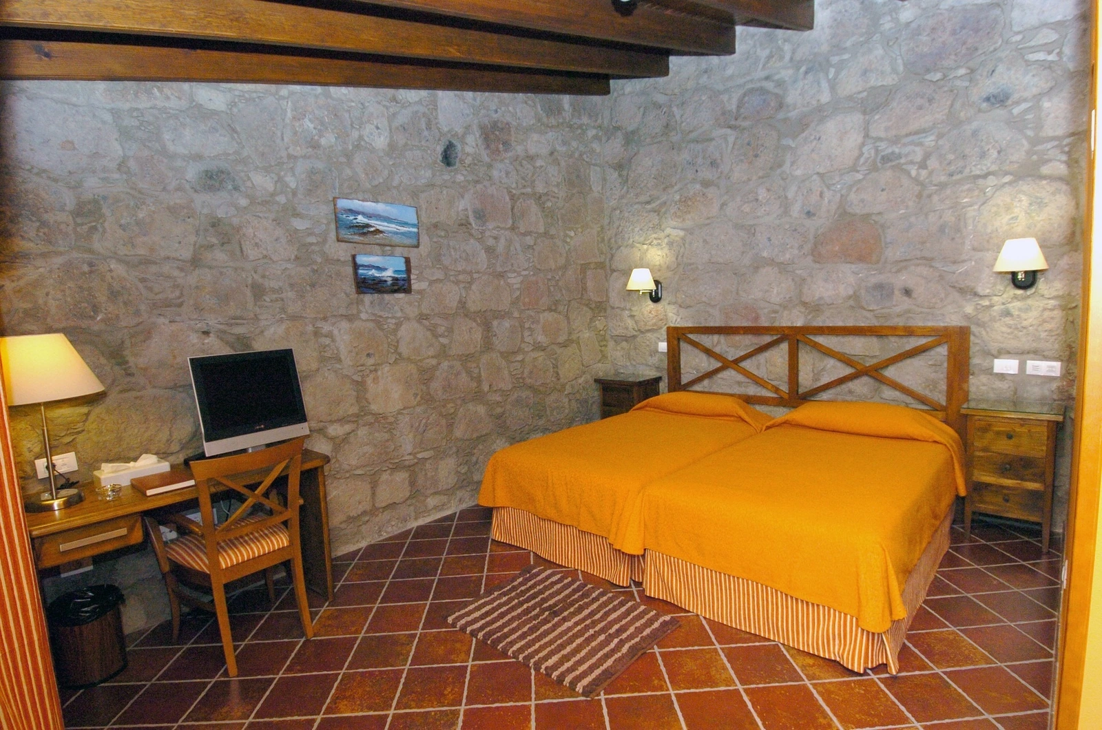 Habitación del hotel con pared de piedra y colcha naranja · Hotel Rural Fonda de La Tea