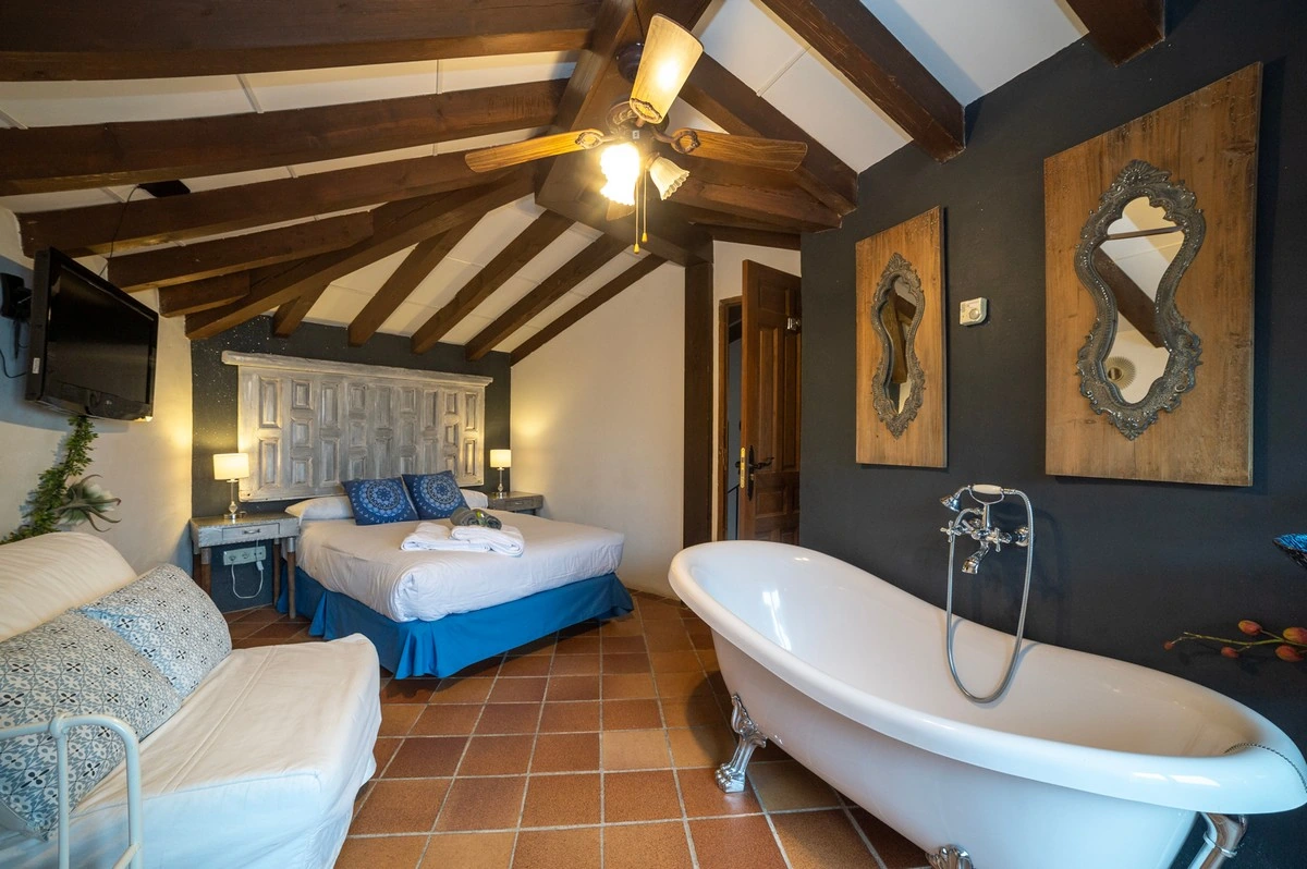 Dormitorio de buhardilla con cama doble y bañera exenta dentro de la habitación. · El Pósito de Hita
