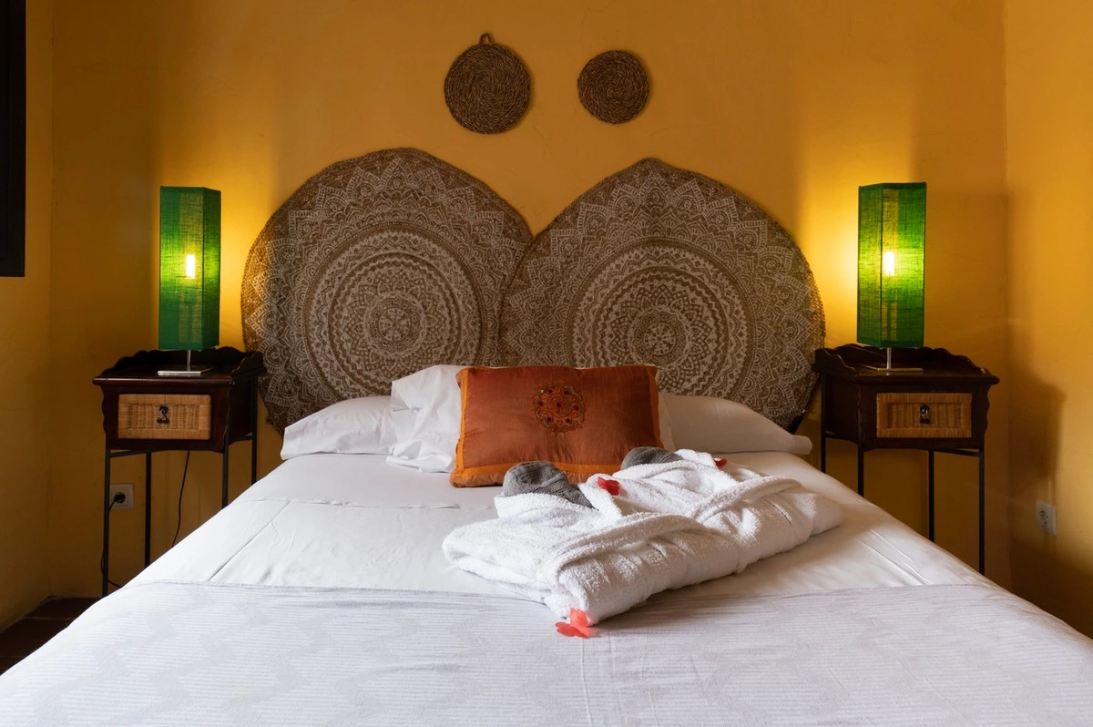 Dormitorio con cama doble, pared ocre y cabecero tallado. · El Pósito de Hita