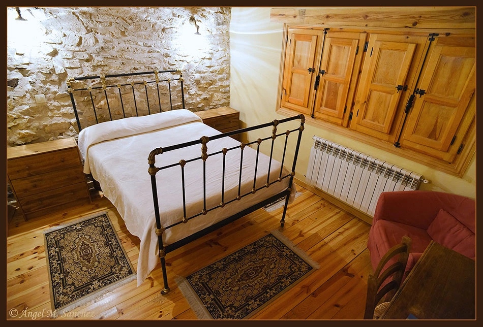 Dormitorio de cama doble con estructura de hierro y pared de piedra. · Las Trojes