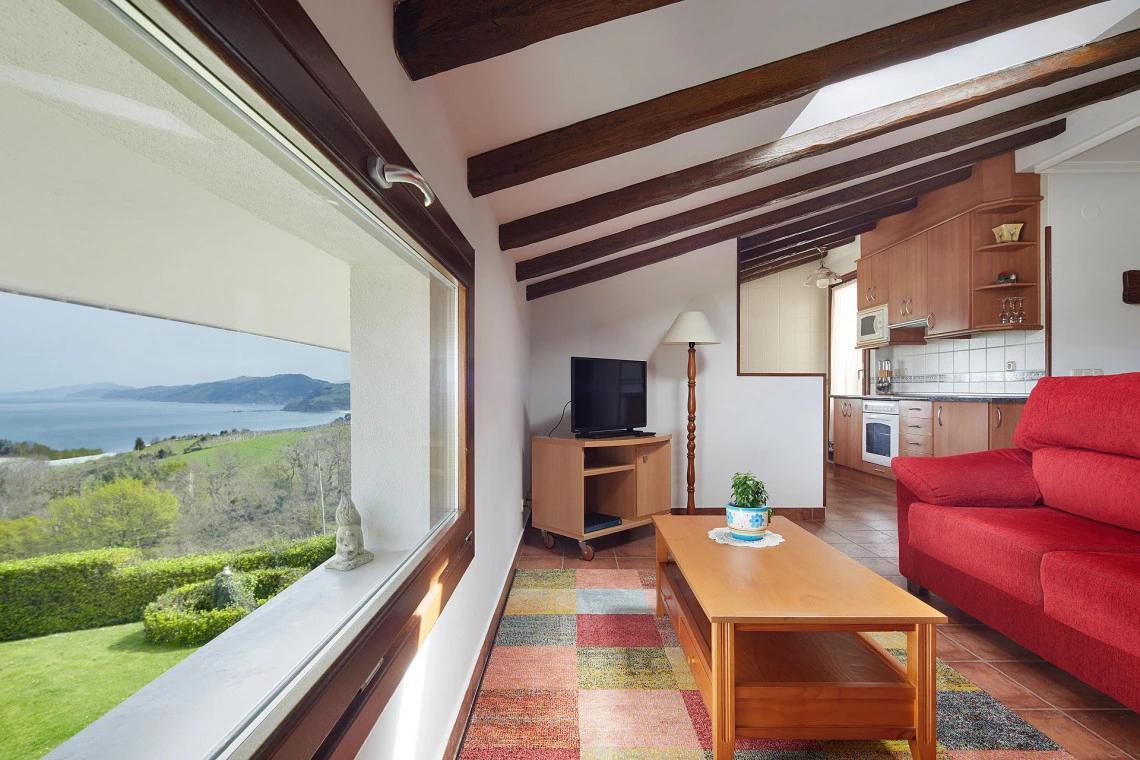 Salón de Itxaso con cocina al fondo y ventanal hacia la costa · Epotx Etxea