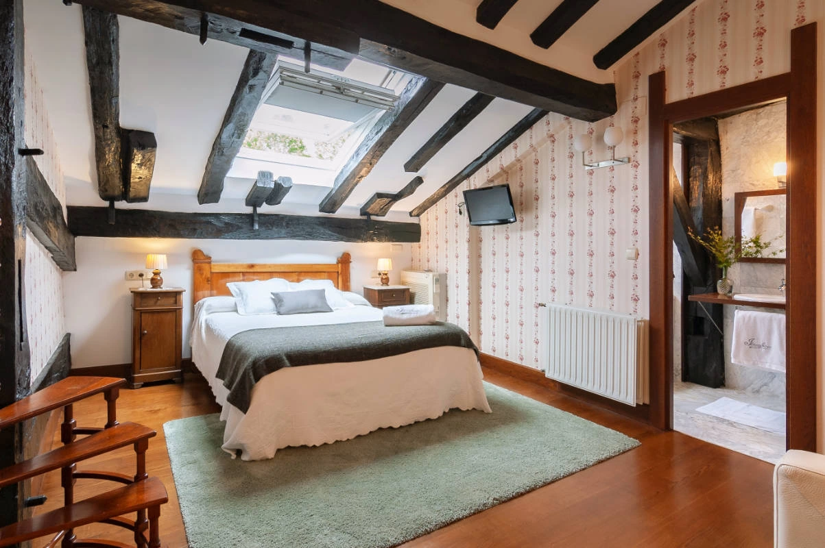 Dormitorio de buhardilla de Jesuskoa con cama doble y parte del baño privado visible. · Jesuskoa