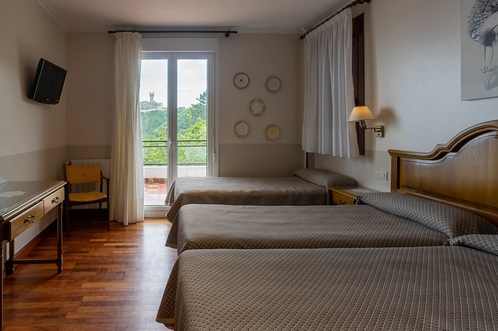 Dormitorio con tres camas y acceso a balcón. · Hotel Leku Eder
