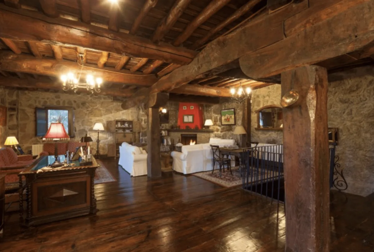 Salón con vigas de madera, muros de piedra y chimenea
